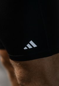 Schwarze Sportshorts aus elastischem Material mit Flachnähten. Mit einem weißen Adidas-Logo auf dem linken Oberschenkel.