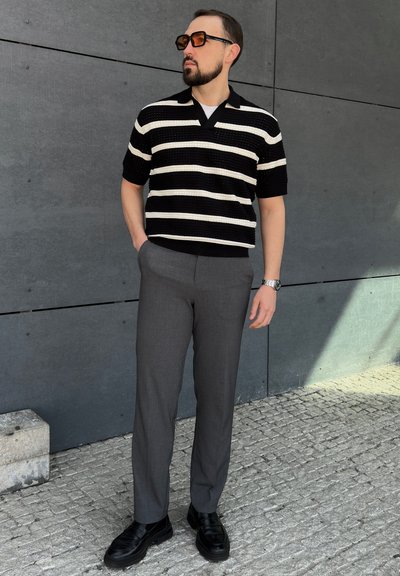 Polo de punto a rayas en blanco y negro con mangas cortas, combinado con pantalones grises de corte entallado y zapatos negros tipo mocasín.