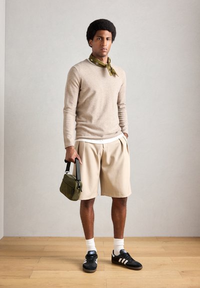Suéter beige, bufanda verde con estampado, pantalones cortos de crepe color crema, zapatillas negras con rayas blancas y bolso verde con bandolera.
