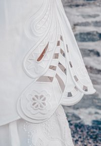 HVIT plagg med intrikate utskjæringer og bølgete kanter. Teksturert stoff med blomster mønstre og detaljerte sømmer.