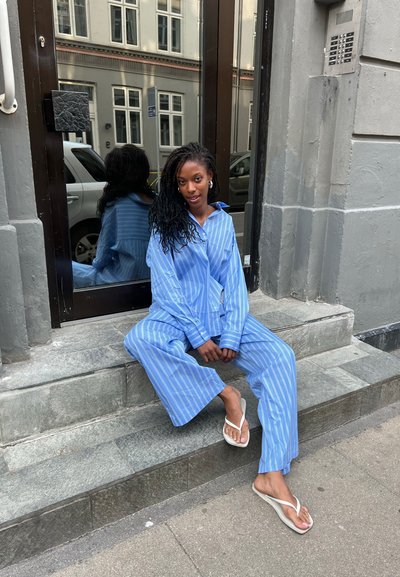 Conjunto de pijama con rayas azul claro, pantalones holgados y camisa de manga larga. Las pantuflas son blancas y un espejo refleja el área circundante.