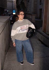 Sivi in beli oversized pulover z napisom "SELF Originals", v kombinaciji z širokimi jeans hlačami in črno torbo na ramah na mestni ulici.