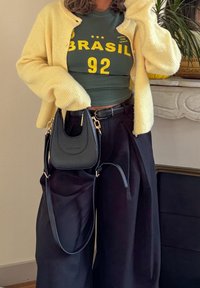 Yellow ribbed cardigan over a dark green shirt with yellow text, paired with high-waisted black trousers and a small black handbag.