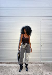Body nero, jeans patchwork grigi e grigio chiaro, stivali neri a punta e una borsa nera, su uno sfondo testurizzato grigio chiaro.