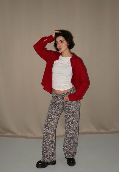 Cárdigan corto rojo sobre una camisa blanca ajustada, combinado con pantalones de pata de elefante de estampado de leopardo y botas de plataforma negras. Tejido suave con patrones notables.
