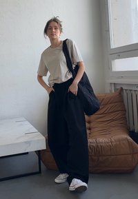 Beige t-shirt, loose black pants, and black tote bag. White sneakers. Simple design, relaxed fit, smooth fabric, and minimal accents.