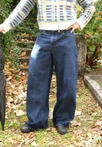 Tumesinistes toonides laia säärega teksapüksid, millel on kõrge vöökoht ja lõdvestunud istuvus. Sobitatud mustriga kampsuni ja mustade jalanõudega.