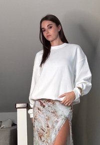 Vit oversized sweatshirt med rund hals, ihopparad med en ljus, mönstrad kjol med hög slits upp till låren i jordnära färger.