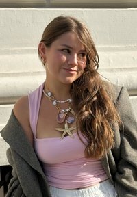 Roze mouwloos topje gecombineerd met een grijze oversized cardigan, versierd met een statement ketting met schelpen en een gouden zeester.