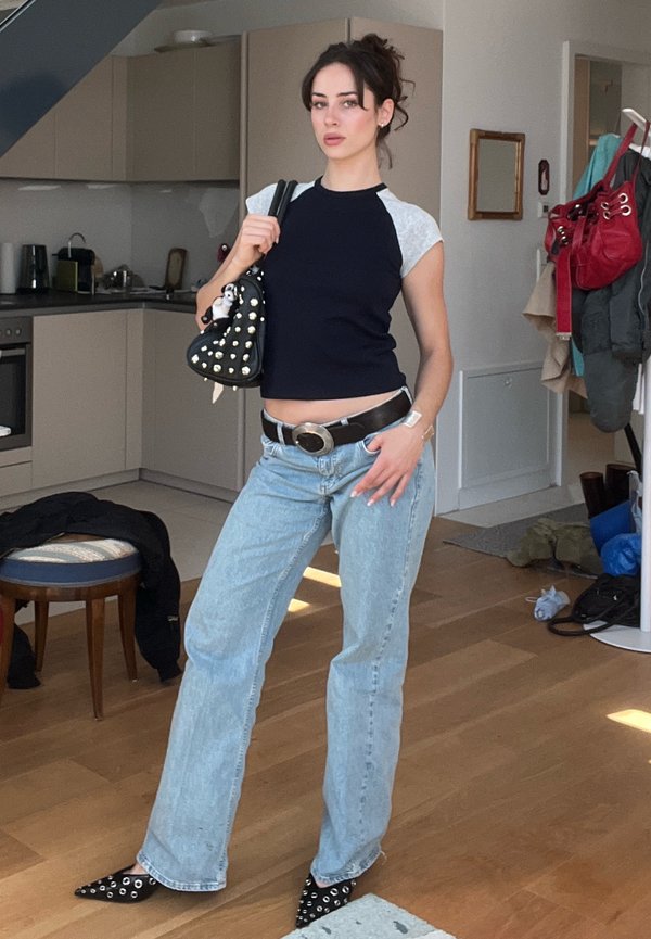 Svart och grå färgblockerad åtsittande topp, ljusblå raka jeans, svart nitat handväska, svarta nitat spetsiga skor. Trägolv som bakgrund.