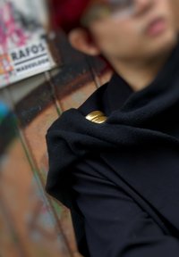 Ein Kleidungsstück aus schwarzem Stoff liegt über der Schulter und ist mit zwei glänzenden goldenen Knöpfen verziert. Die Textur wirkt glatt und weich.