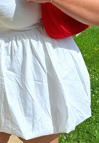 Λευκή, πλισέ φούστα με υφή, σε συνδυασμό με κόκκινη τσάντα. Η φούστα διαθέτει συγκεντρωμένη μέση και είναι μήκους μέχρι το γόνατο.