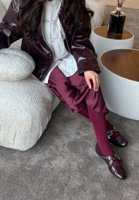 Bordeaux leren jack, witte shirt met rode lijntekeningen, bordeaux satijnen shorts, passende kousen en versierde bordeaux klompen met hardware accenten.