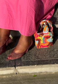 Rot transparente High Heels mit spitzem Zehenbereich, kombiniert mit einer bunten Perlen-Handtasche, die verschiedene Texturen und eine Mischung aus leuchtenden Farbtönen zeigt.