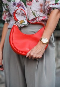 Crvena kožna Furla torba s okruglom siluetom i kratkom ručkom. Ima naglašene srebrne dijelove i logo sprijeda.