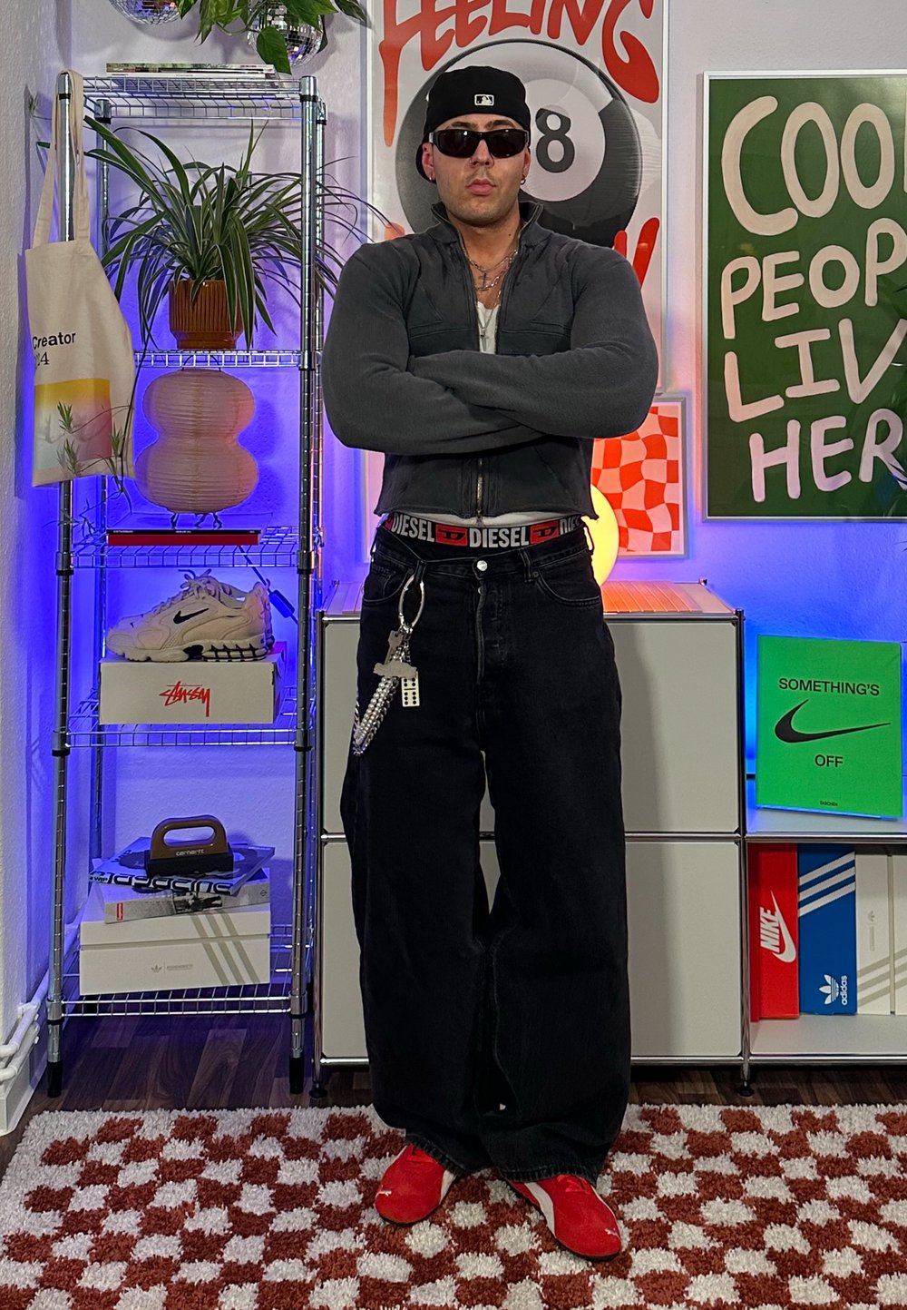 Μαύρα υπερμεγέθη τζιν με κόκκινη ζώνη, γκρίζα ζακέτα με φερμουάρ και κόκκινα αθλητικά παπούτσια. Το μοντέλο φοράει γυαλιά ηλίου και καπέλο baseball. Διακοσμητικό φόντο.