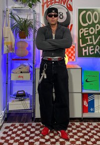 Μαύρα υπερμεγέθη τζιν με κόκκινη ζώνη, γκρίζα ζακέτα με φερμουάρ και κόκκινα αθλητικά παπούτσια. Το μοντέλο φοράει γυαλιά ηλίου και καπέλο baseball. Διακοσμητικό φόντο.