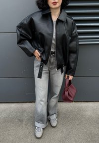 Giubbotto bomber in pelle nera con spalle oversize, jeans grigi con orlo svasato, sneakers grigie e borsa bordeaux.