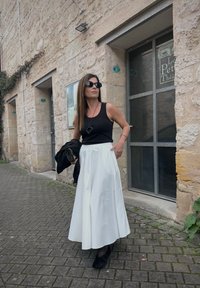 Black tank top with a white midi skirt, complemented by a black blazer and handbag. Sunglasses and a pendant necklace finish off the ensemble.
