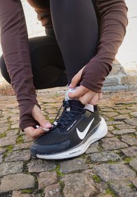 Fekete sportcipő fényvisszaverő részletekkel, texturált felsőrészel és fehér swoosh logóval. Az egyedi fűzőrendszer kézzel állítható.