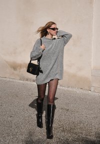 Sivi oversized pulover haljina, crne tajice s točkicama i čizmama do koljena u crnoj boji. Mala crna torbica s zlatnim detaljem.