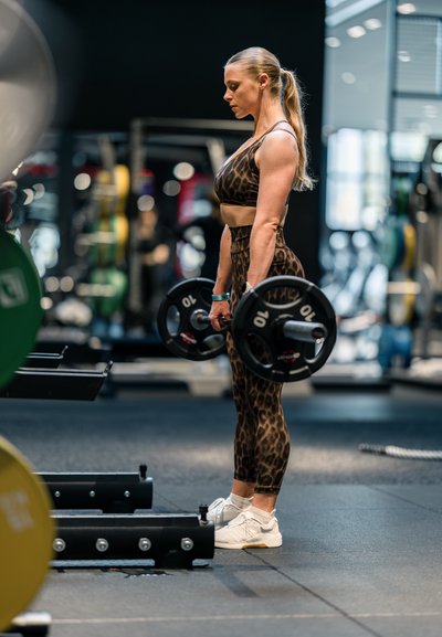 Mujer con ropa deportiva de estampado de leopardo levantando una barra con pesas en un gimnasio.