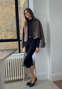 Barna kockás cropped dzseki gombokkal egy fekete garbó és fekete, testre simuló nadrág felett, fekete lapos cipővel és egy kis táskával párosítva.