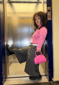 Sive široke hlače, ružičasta majica dugih rukava, crne platforme čizme i mala ružičasta torbica u metalnom dizalu.