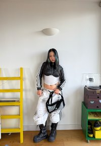 Must musta lühike jakk soonikkoes detailidega, valge tanktop, kulunud valged püksid, läikivad mustad platvormkinnastega saapad ja musta võrkmaterjalist käekott.