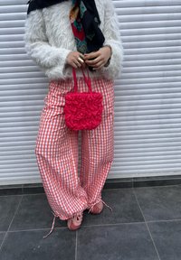 Suéter branco felpudo, calças baggy xadrez vermelhas e brancas, bolsa rosa com babados e calçado rosa sobre uma superfície sólida.