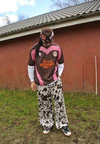 Jersey deportivo marrón y rosa con el texto "ibiza mamma mia", combinado con pantalones de patrón de vaca en blanco y negro y zapatillas negras.