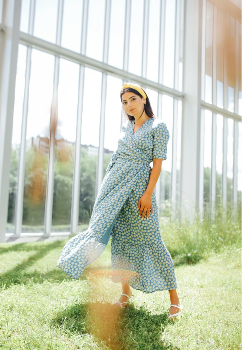 Kék virágmintás ruhászerű ruha, térd fölé érő hosszúságban, rövid ujjakkal, fodros szegéllyel, deréknál megkötve; sárga hajpánttal kiegészítve.