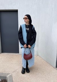 Τζιν γιλέκο πάνω από ένα μαύρο φούτερ, ανοιχτό μπλε φούστα, μαύρες μπότες και κόκκινη τσάντα. Αξεσουάρ περιλαμβάνουν γυαλιά ηλίου και στρωτές αλυσίδες.