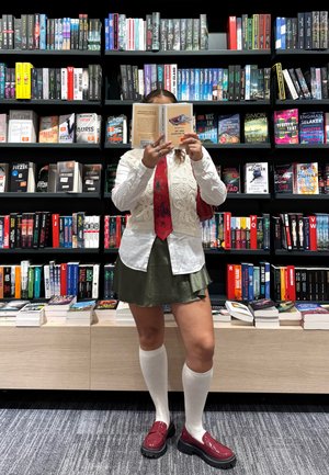 Chaleco de punto sobre una camisa blanca, corbata roja con patrón floral, falda verde oliva, medias blancas hasta la rodilla y mocasines burdeos brillantes.