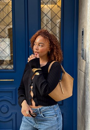 Black ribbed cardigan with a V-neck and button closure, paired with light blue jeans and a beige handbag. Gold accessories add detail.