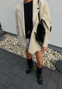 Bež oversized blejzer preko črne srajce, v kombinaciji z belo krilo in črnimi škornji do kolen. Črna torba in okrogla srebrna ogrlica sta vključena.