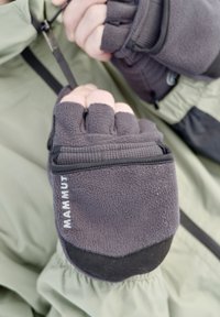 Des mains portant des gants gris sans doigts Mammut, ajustant un cordon noir sur la manche d'une veste verte.