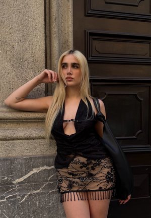 Top negro de tirantes con un escote en V profundo, tejido texturizado, combinado con una falda sheer beige que presenta bordados florales y acentos de flecos de cuentas.