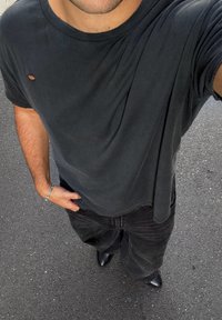 Čierne oversized tričko s malým otvorom na hrudi, skombinované s čiernymi širokými džínami a elegantnými čiernymi čižmami, na pozadí dlažby.