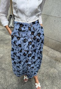 Γαλάζια φλοράλ φούστα με μαύρα και πορτοκαλί λουλούδια, με κουμπιά μπροστά και τσέπες, σε συνδυασμό με λευκά ανοιχτά σανδάλια.