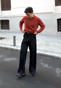Pull en maille couleur rouille à col en V, associé à un pantalon noir taille haute à jambes larges et des chaussures noires, debout dans une rue de la ville.