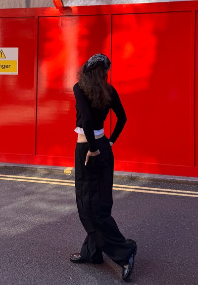 Camiseta de manga larga negra superpuesta sobre una camiseta blanca, combinada con pantalones sueltos negros. Accesorios con una bufanda negra con estampado.