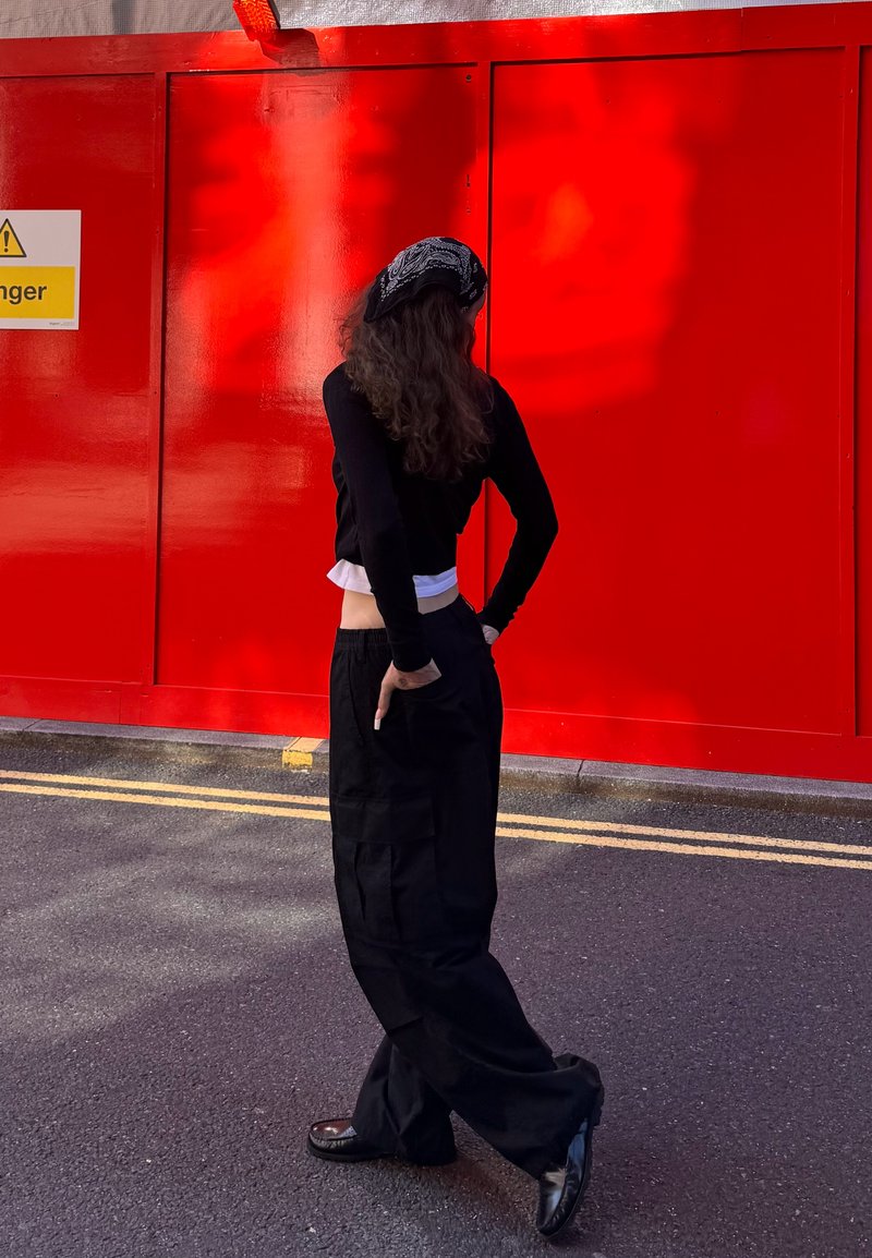Maglietta nera a maniche lunghe indossata sopra una maglietta bianca, abbinata a pantaloni larghi neri. Accessoriata con una sciarpa nera a fantasia.