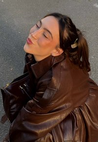 Brun skinnjakke med strukturert design; skinnende tekstur og detaljert søm. Følges av en matchende brun håndveske.