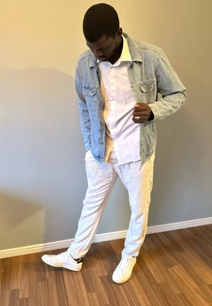 Chaqueta de mezclilla azul claro sobre una camisa blanca abotonada, combinada con pantalones blancos y zapatillas deportivas. El look presenta un diseño casual y un ajuste relajado.