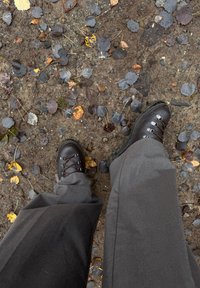 Rudi žygio batai su metalinėmis akytėmis ir rudomis raišteliais. Dėvimi su pilkomis kelnėmis, supami šlapios žemės, numestų lapų ir žvyro.