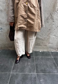 Giacca beige con bottoni, pantaloni larghi in lino crema e scarpe con tacco quadro marrone scuro. Sono evidenti le variazioni di texture e il contrasto di colori.