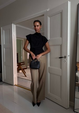 Top negro de cuello alto y pantalones anchos beige, con un pequeño bolso negro. Diseño minimalista, tela suave y tacones negros de punta.
