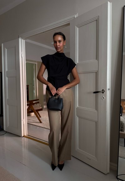 Top negro de cuello alto y pantalones anchos beige, con un pequeño bolso negro. Diseño minimalista, tela suave y tacones negros de punta.