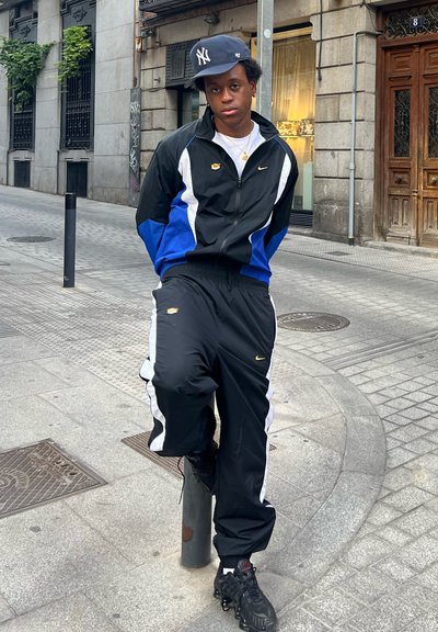 Chándal negro y azul con detalles en blanco y logo de Nike, combinado con zapatillas negras. De pie contra un fondo urbano.
